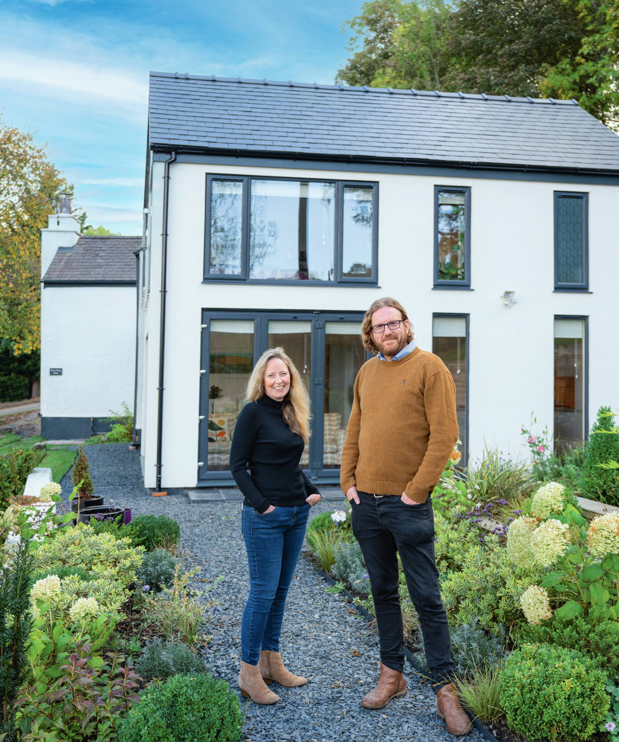 Homeowners in garden in front of white stone cottage with modern extension in Wales