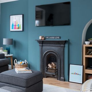 A teal-painted living room with the TV placed above a black fireplace