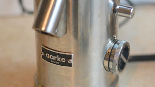 Image of the Aarke Coffee System – a stainless steel coffee bean grinder and drip coffee maker – positioned on a kitchen counter