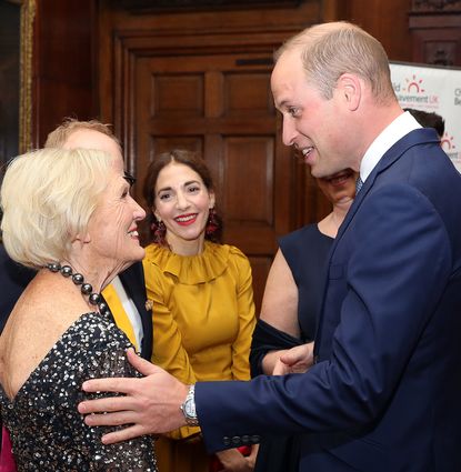 Mary Berry wearing a sequin dress, smiling at Prince William who is touching her arm