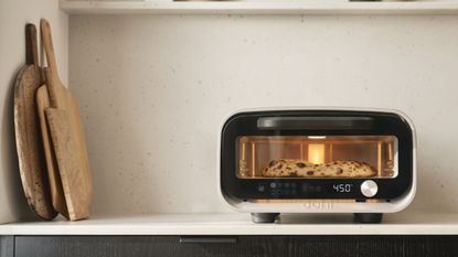 Black pizza oven on white countertop next to three wooden cutting boards