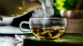 Peppermint tea being poured from steaming teapot into glass cup