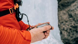 Close up of an ice climber testing an avalanche transceiver beacon before climbing a frozen waterfall