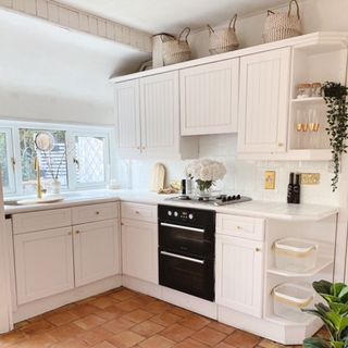Kitchen with white cupboards and built-in oven and hob with glass vase with roses on top of hob