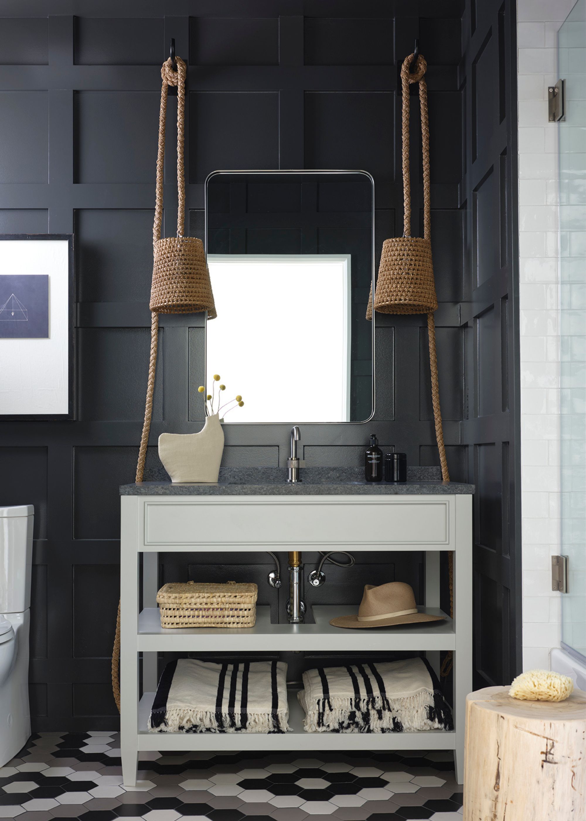 A bathroom with black shaker-style wall paneling and a cabinet with a sink built in, and rustic decor.