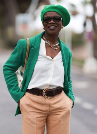 A guest seen wearing a green hat, black sunglasses, a white blouse, a green blazer, beige pants and black loafer shoes during the 76th Cannes film festival on May 21, 2023 in Cannes, France