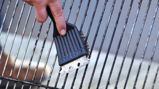A close up of a hand cleaning a grill with a grill brush
