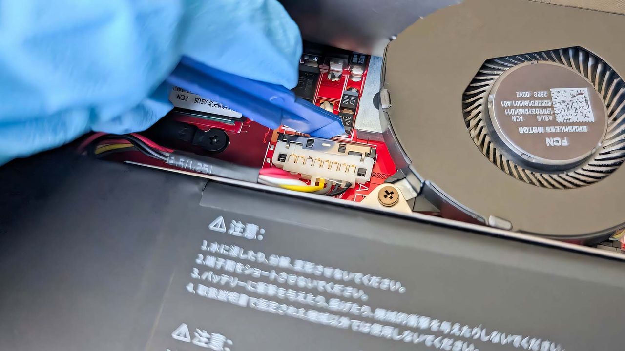 A gloved hand using the JSAUX ROG Ally Battery Upgrade Kit prying tool to reattach the battery cable.