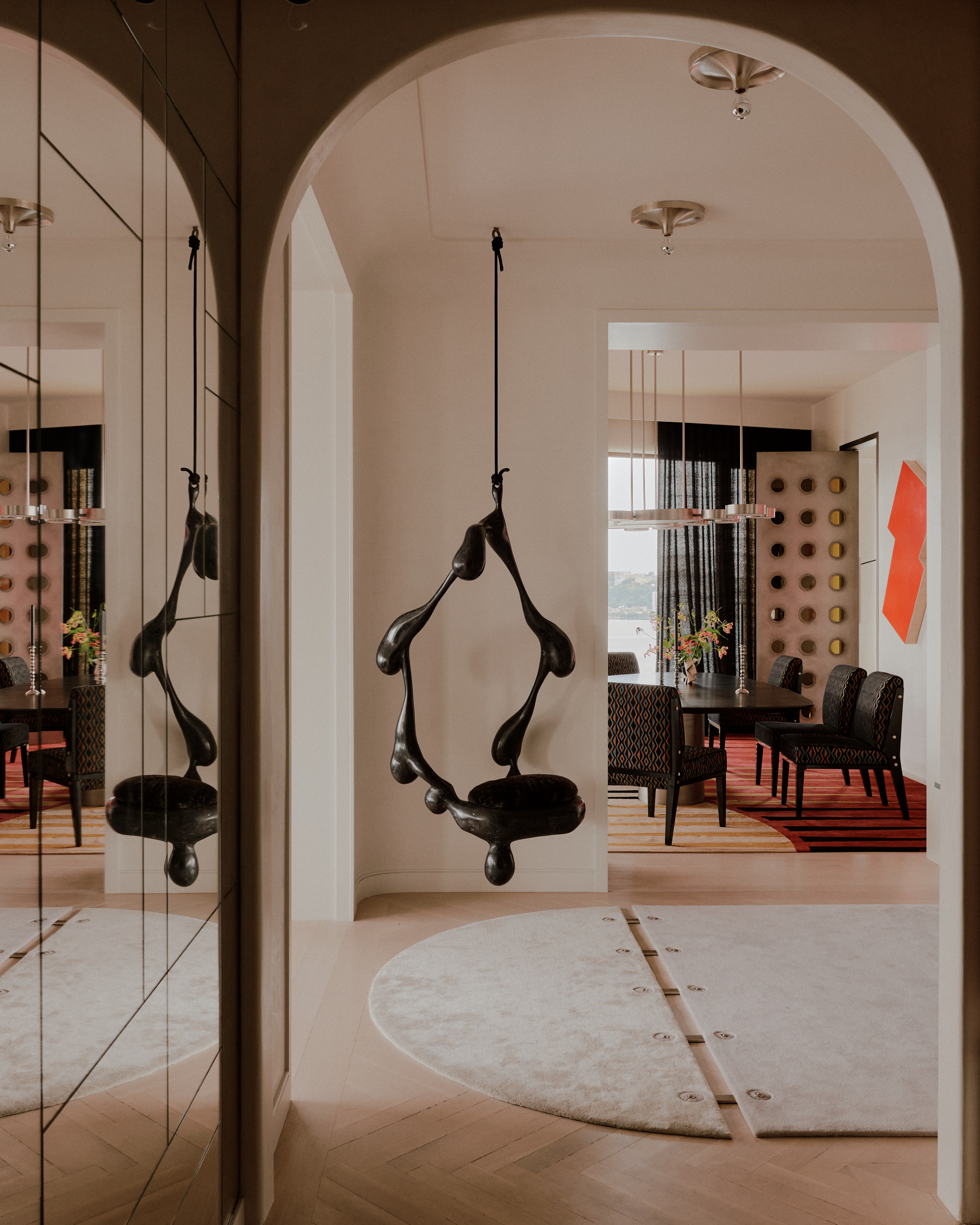modern entryway with mirrored wall, arched door frame, curved rug, sculpture hanging from ceiling, and views through to the dining room