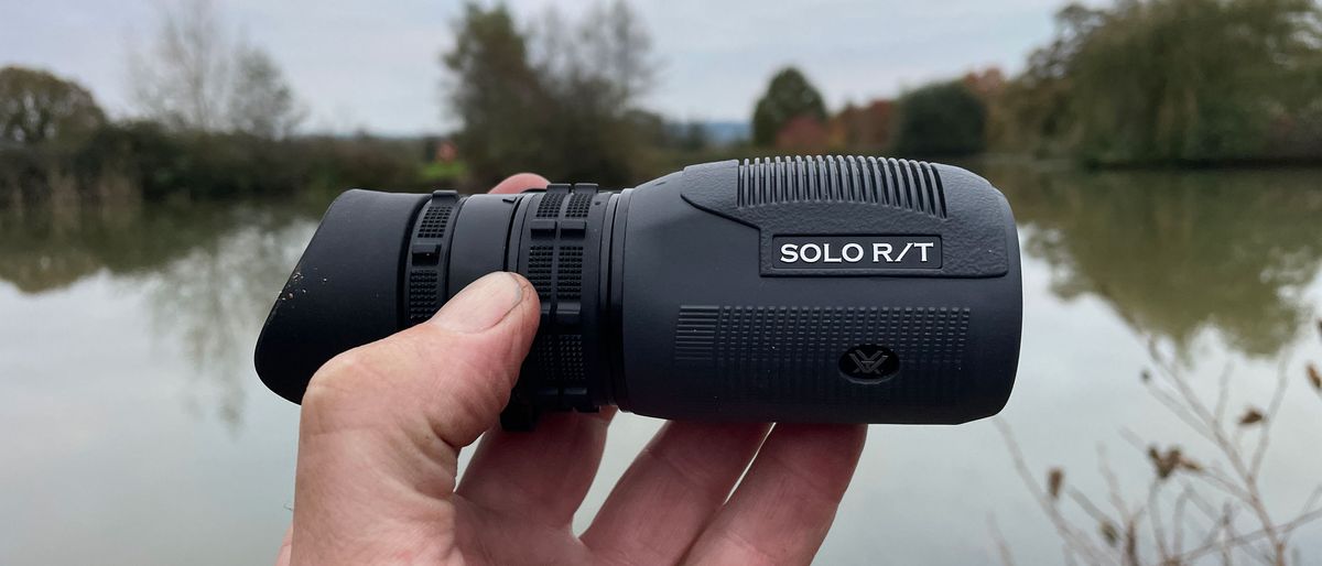 Hand holding Vortex Solo R/T 8x36 monocular in front of a lake.