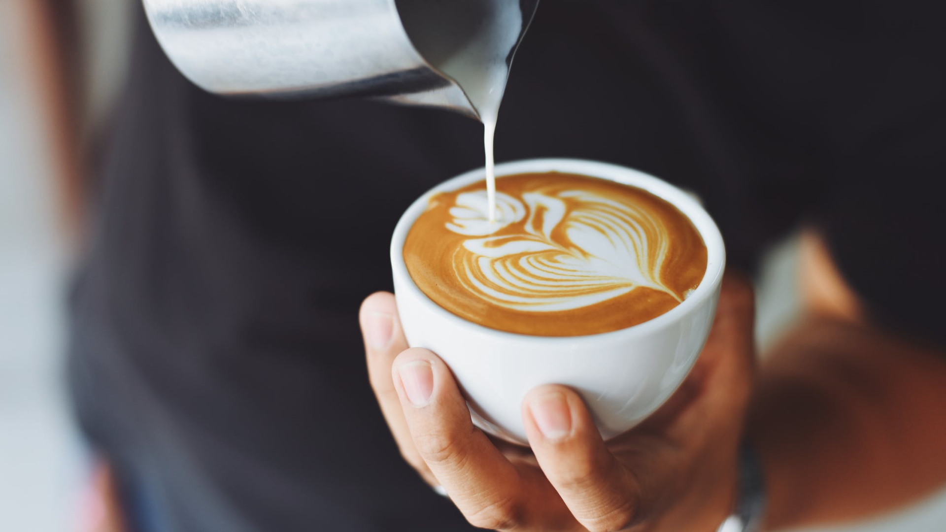 A person pours milk into a cafe