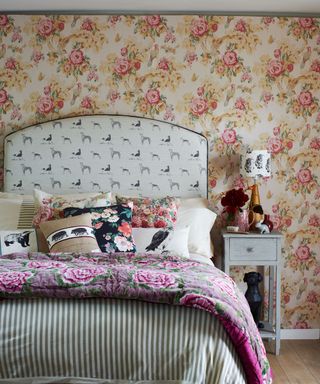 A bohemian country bedroom with floral pink wallpaper, striped and animal motif bedding and lots of cushions