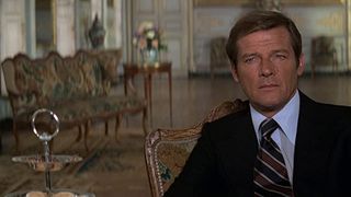 Roger Moore sits down in a palace room and stares at someone off screen in Moonraker