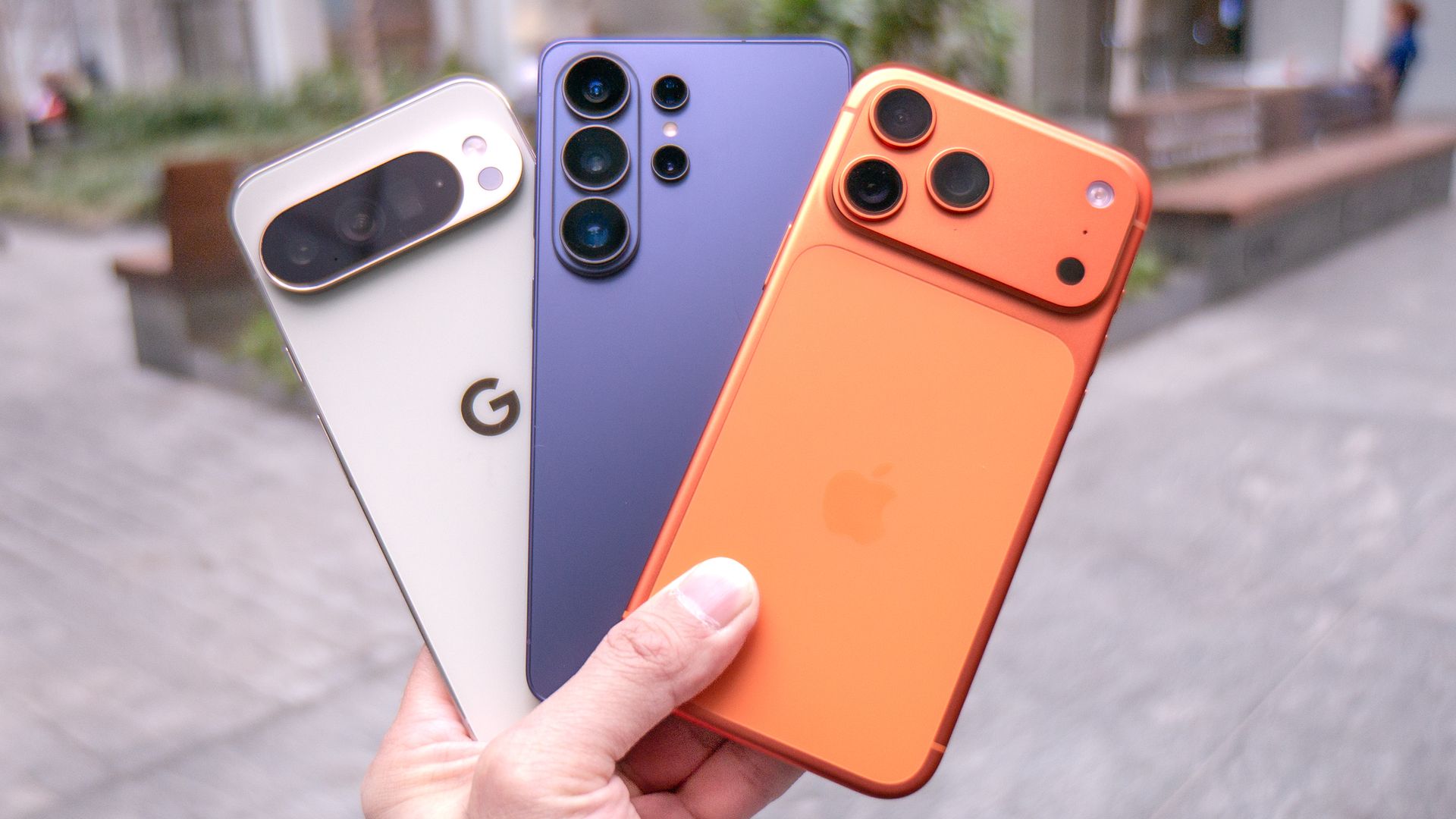 A Google Pixel 10 Pro XL, Samsung Galaxy S26 Ultra and iPhone 17 Pro Max displayed in a fan in a user's hand