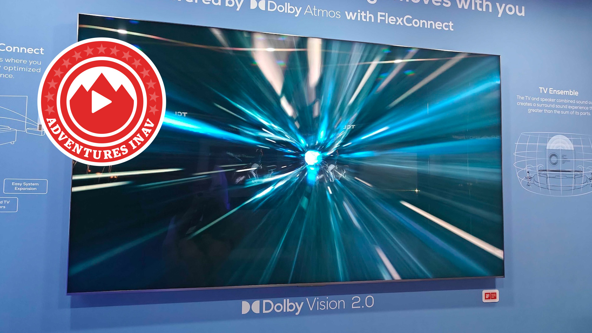 A large TCL TV photographed against a blue wall. In the corner of the photo is a red logo with the words 'Adventures in AV'