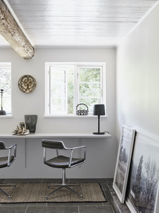 farmhouse decor ideas in a white home office space, desk on wall with two metal and black leather desk chairs, stone flooring