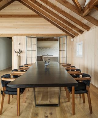 A dining room with oak-clad walls, beamed ceiling, dark wood table and dining chairs with black leather seats