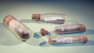 four corked glass vials each containing reddish-brown rock and dust