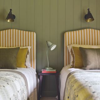 twin bedroom with single beds with striped upholstered headboards, welsh blankets and brass wall lights