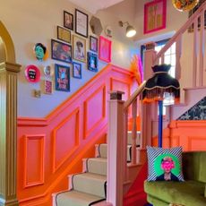 Very bright hallway with a small sofa and a lamp with orange panelled staircase 