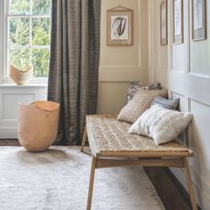 Panelled living room with a rattan bench with cushions on it, sitting on a cream rug 