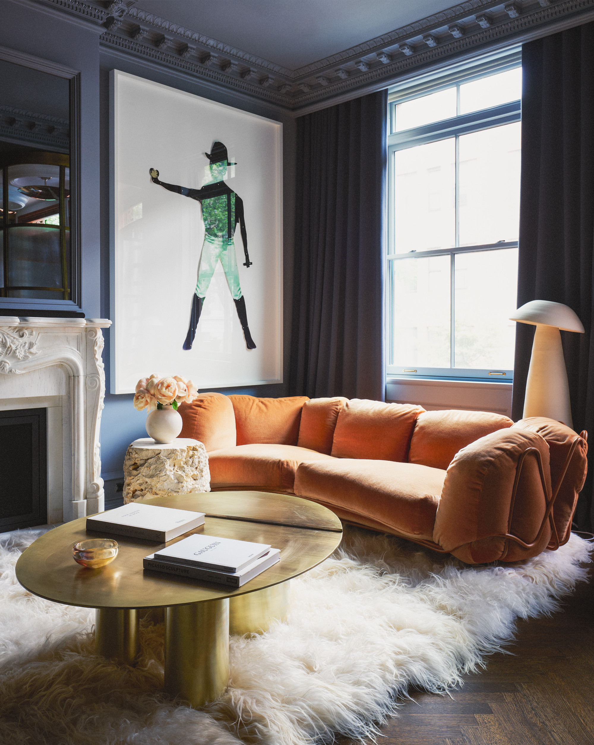 Navy living room with orange curved sofa, large figurative artwork, brass round coffee table, fluffy cream rug and white floor lamp
