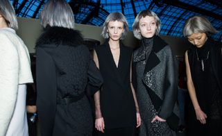 2 Models wearing black open chest blouse, and grey/black coat with matching dress