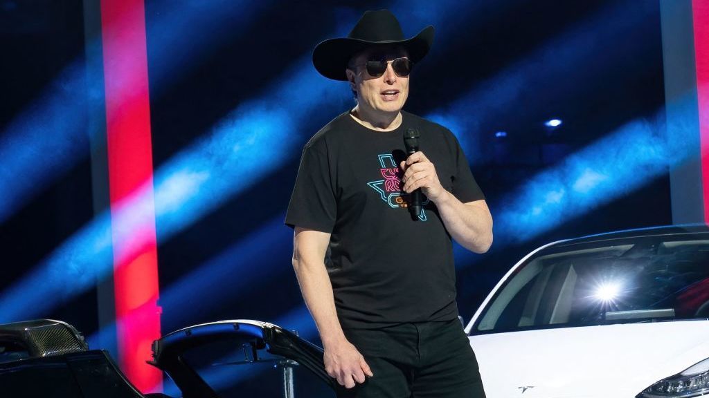 Elon Musk wearing a cowboy hat in front of a Tesla