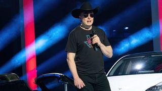 Elon Musk wearing a cowboy hat in front of a Tesla