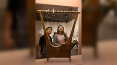 Two people look at an ancient wooden lyre on display at a museum