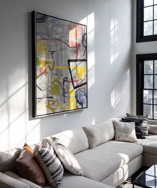 living room with white sectional sofa, white walls and bright contemporary artwork. Black framed double height windows