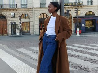 European influencer Sylvie Mus poses in Paris wearing a camel coat, white T-shirt, and jeans.