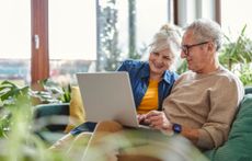 A smiling senior couple sits on the couch, working on Medicare open enrollment.