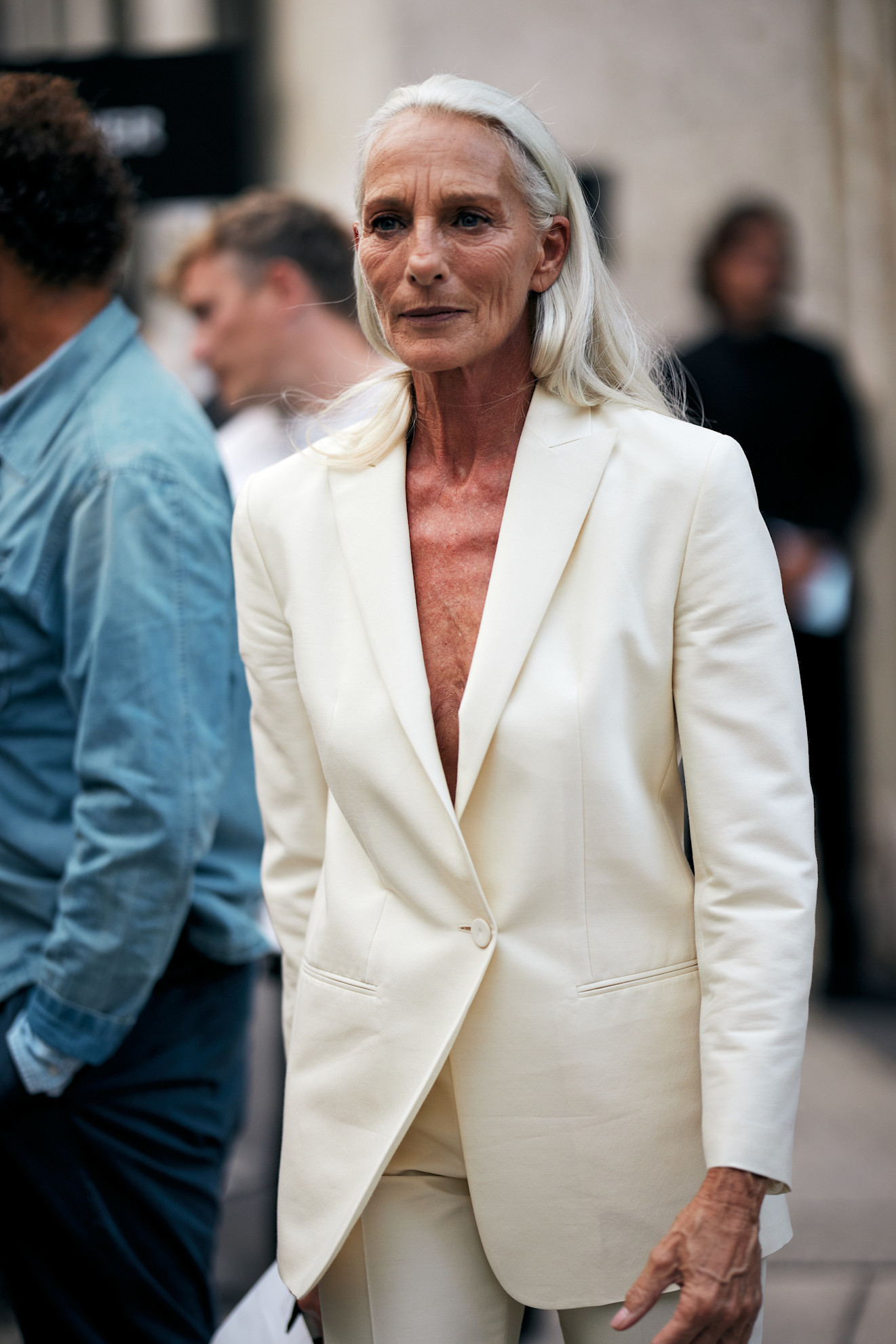 a woman with tan skin and silver hair wearing a low cut white suit jacket