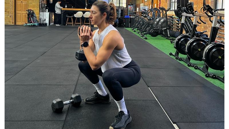 Jess performing a goblet squat holding one dumbbell in both hands and sitting down into her squat