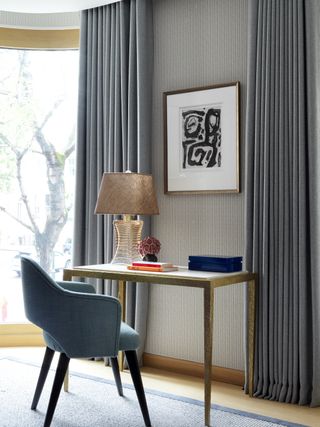 home office with gold desk, blue chair, artwork, blue/gray drapes, rug, lamp