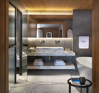bathroom with marble vanities, basin and floor, wooden ceiling, white bath, large mirror, glass doors