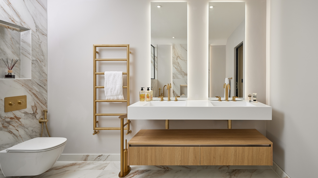 Marble bathroom with fluted wooden cabinetry, double sinks and copper brassware. 