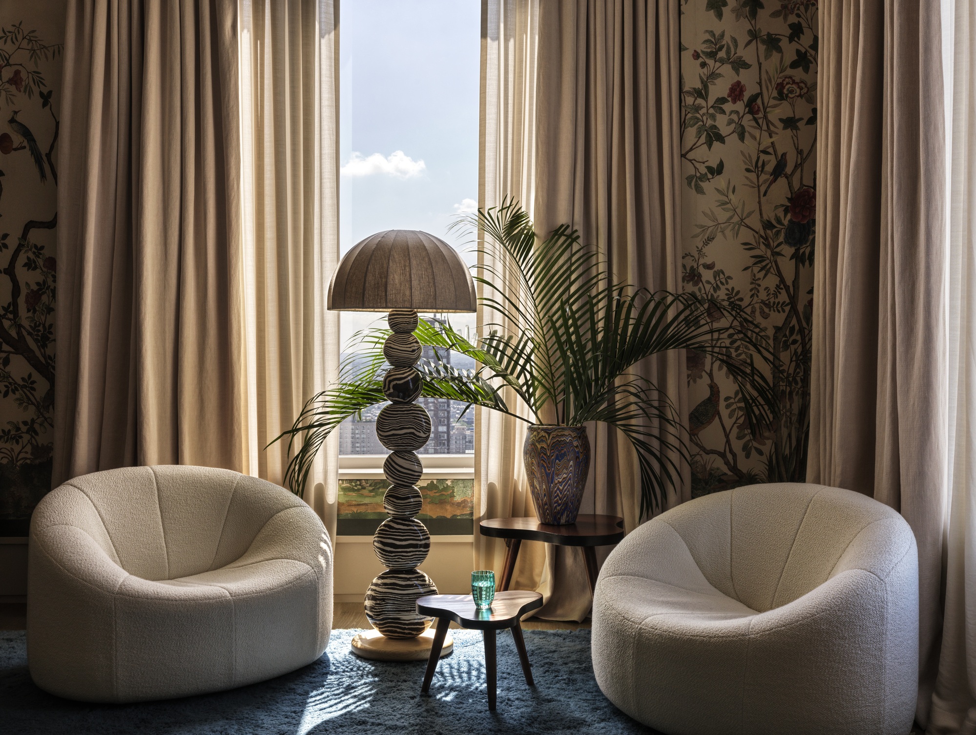 living room with heavy curtains, blue carpets, ceramic floor lamp, two boucle armchairs, patterned floral wallpaper