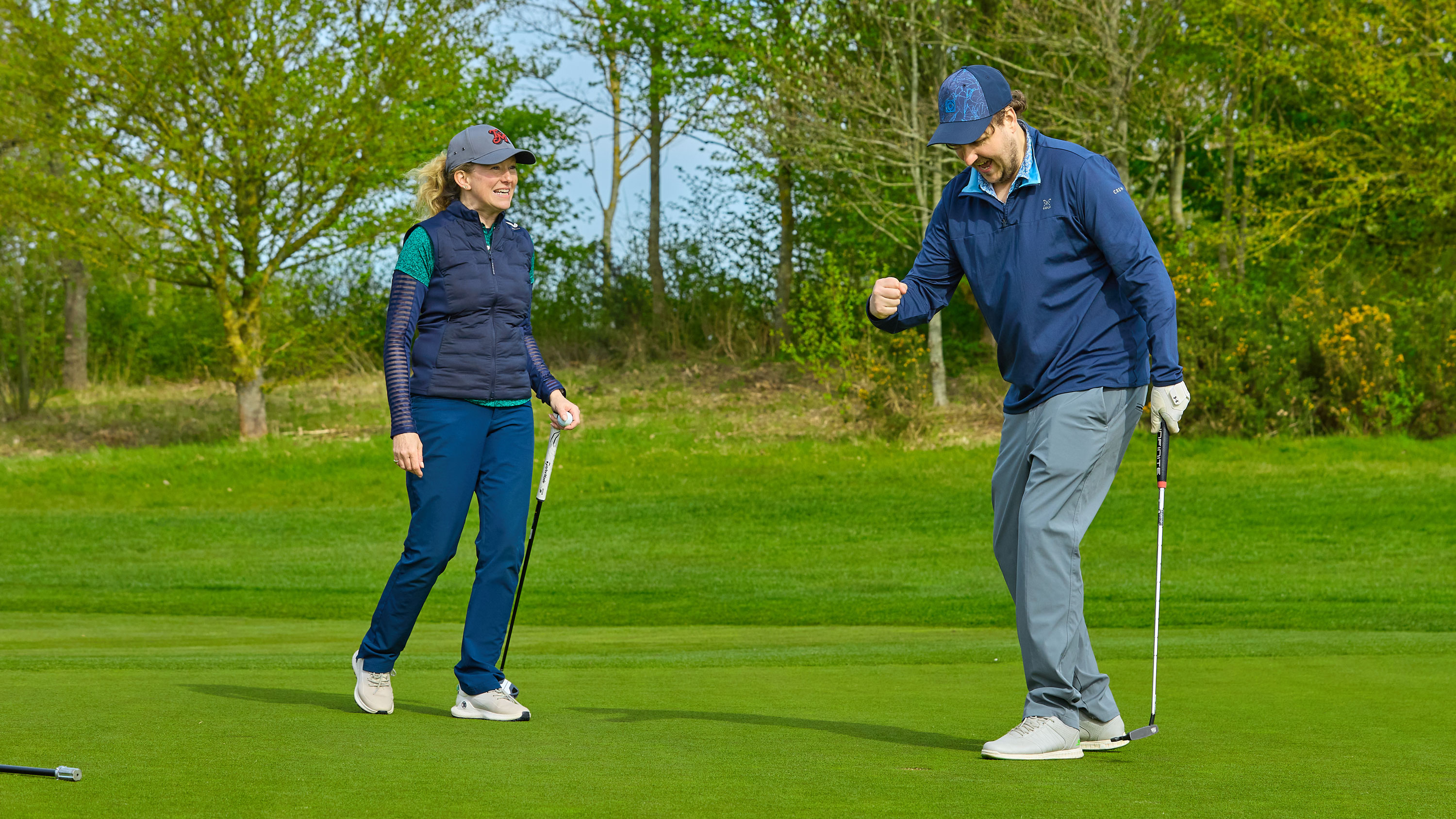 a golfer gives a fist-pump after holing a putt while a playing partner behind looks happy