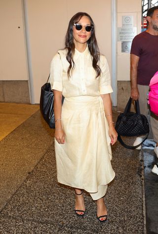 Rashida Jones wears a light yellow button-down shirt and matching midi skirt.