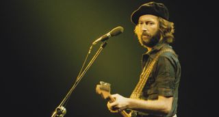 Eric Clapton wears a beret and plays a Fender Stratocaster onstage.