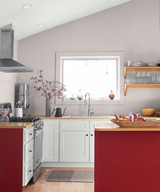 A kitchen with white cabinet fronts, red cabinet sides and island, and a lilac wall