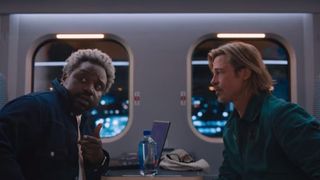 Brad Pitt and Brian Tyree Henry sit across each other in a train in Bullet Train