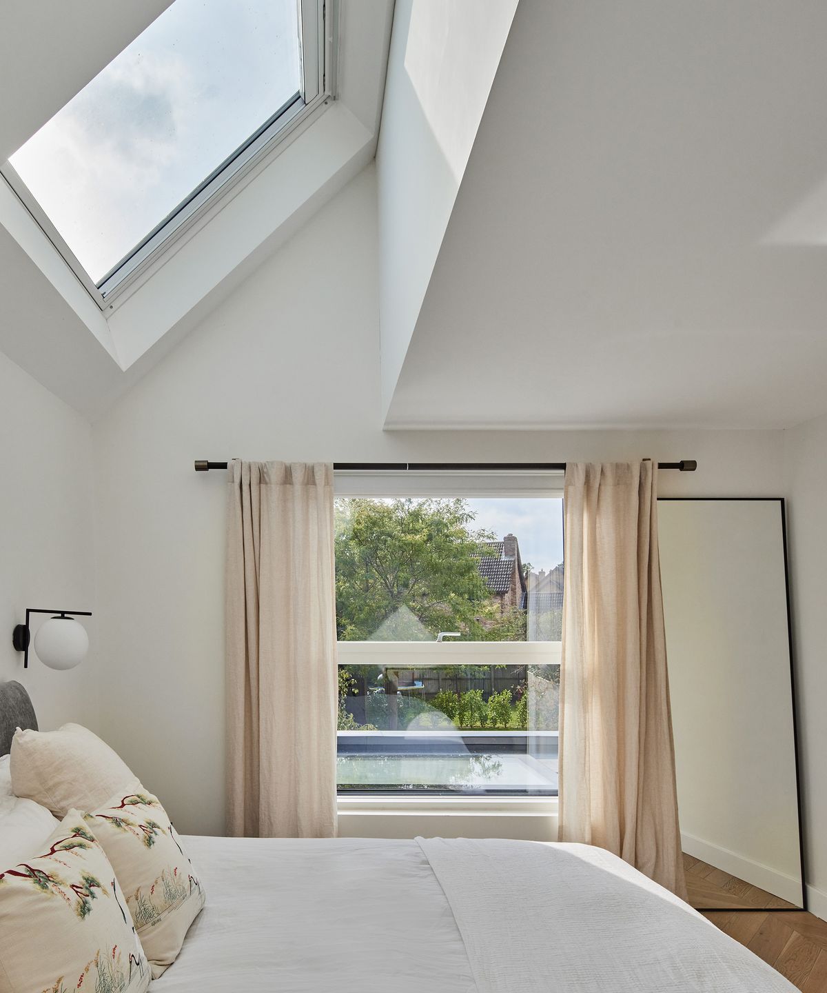A clean and contemporary bedroom in a new build home. There is a pitched roof with large roof light and window looking out to the garden