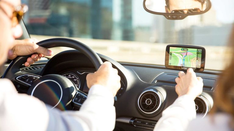 A man and woman driving in a car, looking at one of the best sat navs on the dash board from TomTom