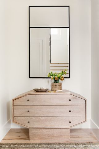 bedroom chest of drawers in an alcove with mirror above, vase of flowers, rug, trinket bowl