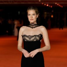 Meghann Fahy on a red carpet wearing a black gown with lace trim and a lace choker