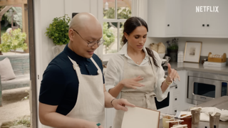 Meghan Markle and Daniel Martin wearing aprons in a white kitchen making candles