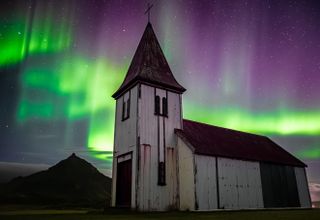 ribbons of green and purple light stretch throughout the sky, in the foreground is white wooden church.